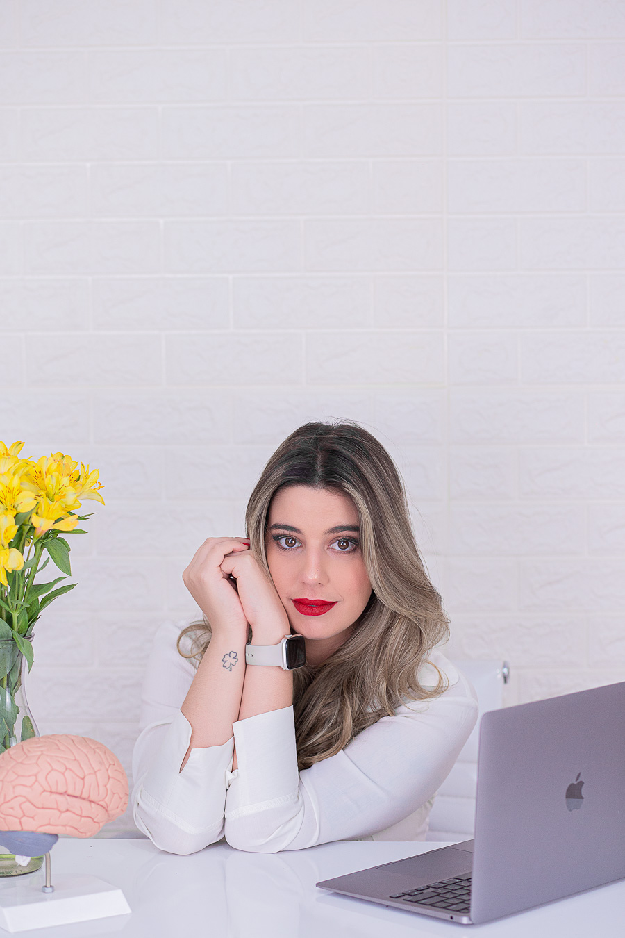 Leticia Teixeira sentada à mesa, com as mãos apoiadas no rosto, ao lado de um notebook