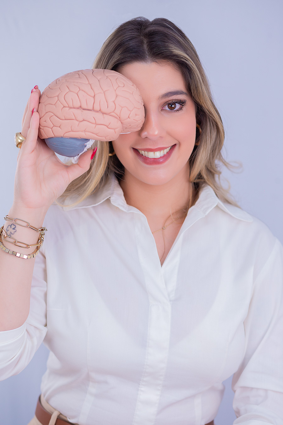 Leticia Teixeira sorrindo com um modelo de cérebro diante do rosto