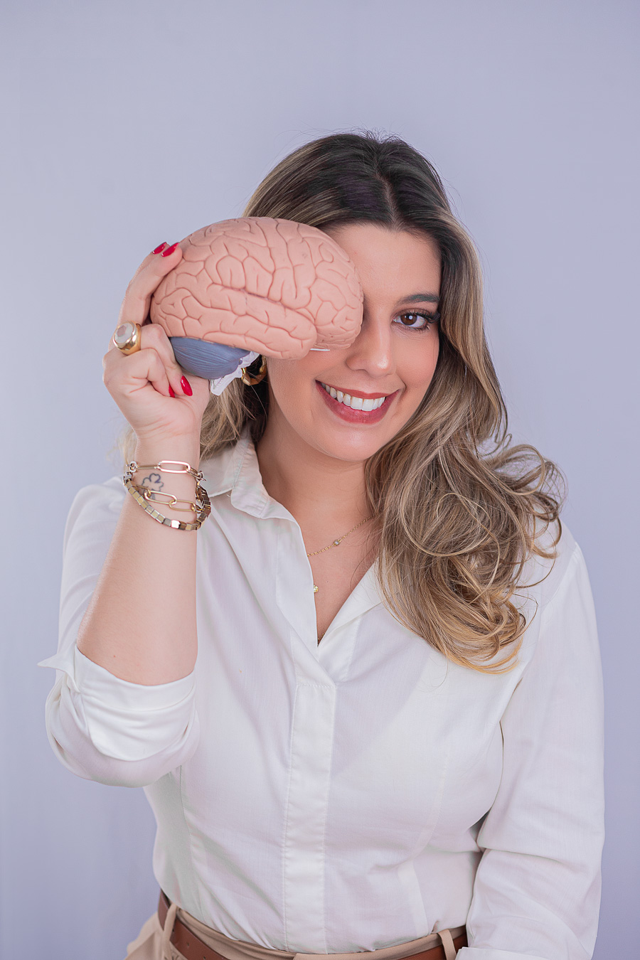 Leticia Teixeira sorrindo e segurando um modelo de cérebro na frente de um dos olhos