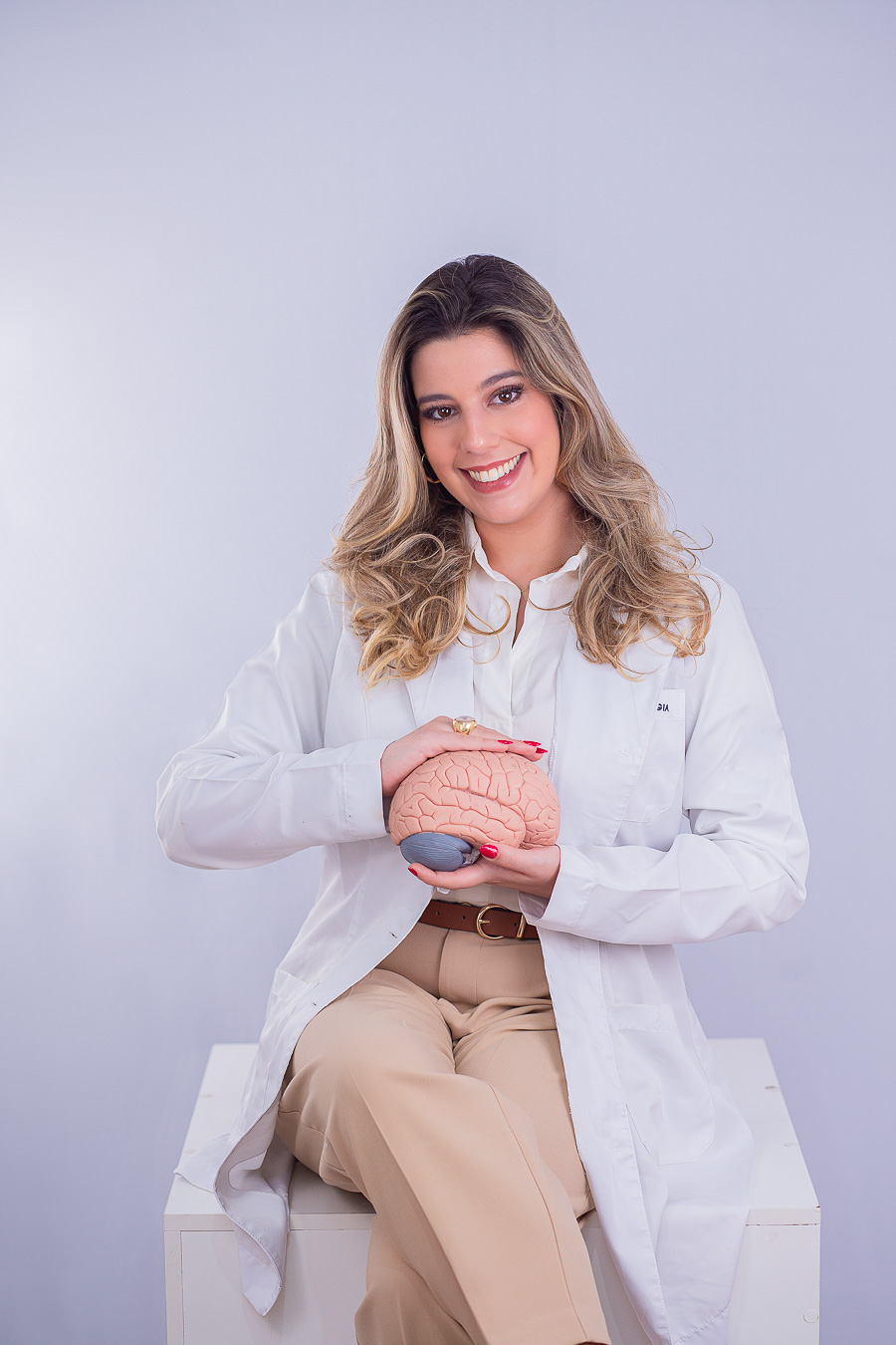 Leticia Teixeira de jaleco, sentada, segurando um modelo de cérebro
